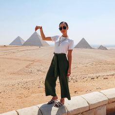 a woman standing on top of a stone wall in front of the giza pyramids