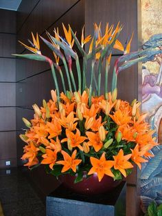 an arrangement of orange flowers in a vase on a table next to a wall painting