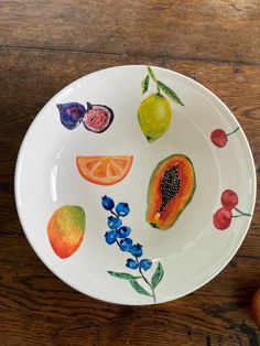 a plate with fruit painted on it sitting on top of a wooden table next to an apple