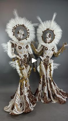 two women dressed in white and gold with feathers on their head, standing next to each other