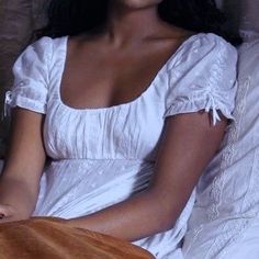 a woman in a white dress is sitting on a bed and smiling at the camera