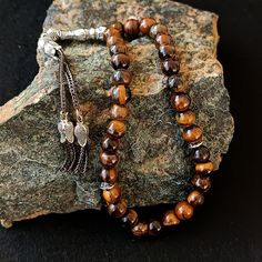 This handmade gemstone tasbih; It is also known by different names such as misbaha, prayer beads, rosary, chapelet, dhikr beads, misbah, sibha. This tasbeeh is a great idea on islamic gift. All beads are Tiger's Eye Gemstone. The known proferties of tiger's eye gemstone are: - It's helpful against overcoming emotions such as fear, stress, and resentment. - It relieves headaches. - It's beneficial for asthma and heart patients Tassel material is stainless metal. PRODUCT DETAILS Grain Shape: Round Traditional Brown Beaded Bracelet With Natural Stones, Traditional Brown Beaded Bracelets With Natural Stones, Traditional Handmade Rosary Bracelet, Traditional Handmade Rosary Bracelet With Round Beads, Traditional Rosary Bracelet With 8mm Beads As Gift, Brown Hand-strung Rosary As Gift, Traditional Rosary Bracelet With 8mm Beads, Brown Natural Stones Mala As A Gift, Handmade Brown Mala As A Gift