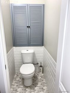 a white toilet sitting inside of a bathroom next to a cabinet with shutters on it