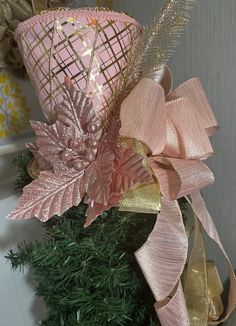 a pink and gold hat on top of a christmas tree with ribbon around the neck