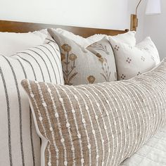 the pillows are lined up on the bed with white linens and brown striped pillow cases