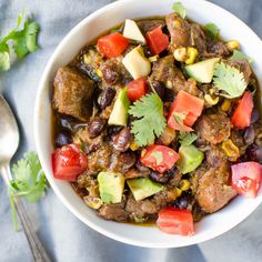 a white bowl filled with meat and veggies next to a spoon on top of a table