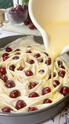 a pan filled with cream and cherries being drizzled on top of it