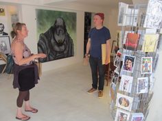 two people standing in an art gallery looking at pictures on the wall and one person holding a bag