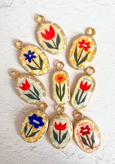 six pendants with flowers painted on them sitting on a white surface, one is yellow and the other is red