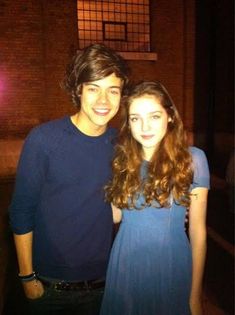 two people standing next to each other in front of a brick building at night time