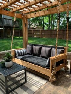 a wooden porch swing with black cushions on it and a coffee table in the foreground