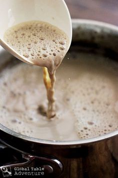 a ladle full of liquid being poured into a pot