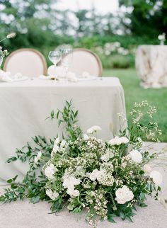 a table with white flowers and greenery is set up for an outdoor wedding reception