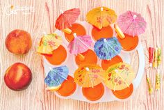 there are many small cupcakes with umbrellas on the plate next to an apple