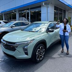 a woman standing next to a green car in front of a blue and white building