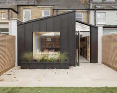 a black building with an open window and plants in the front yard, next to a brick wall