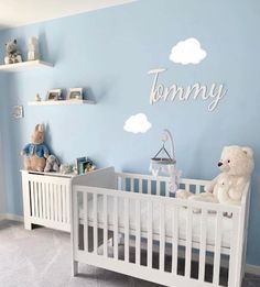 a baby's room with blue walls and white crib, teddy bear and bookshelves