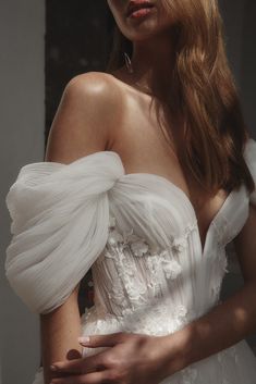 a woman with long hair wearing a white dress and holding her hands on her chest