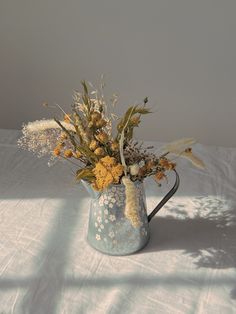 a blue pitcher filled with flowers on top of a white table cloth covered bedding