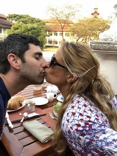 a man and woman kissing each other at an outdoor table