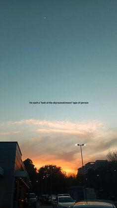 the sun is setting behind some cars parked on the side of the road in front of a building