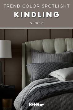 a bed with grey sheets and pillows next to a lamp