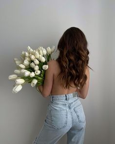 a woman holding a bunch of white tulips in her back and looking at the wall