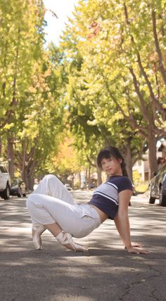 a woman in white pants and black shirt leaning on her knees while riding a skateboard