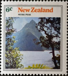 the new zealand postage stamp shows a lake and mountains in the distance, with trees on either side