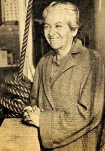 an old black and white photo of a smiling woman in front of a ship's flag