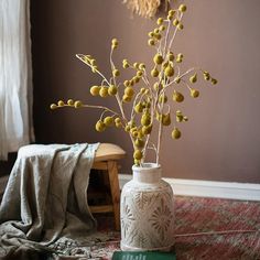 a white vase filled with yellow flowers on top of a rug