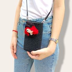 a woman is holding a crocheted purse with a red doll on the front