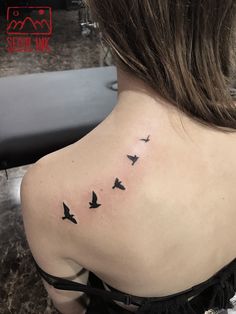 the back of a woman's shoulder with birds flying in the sky on it