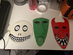 three paper masks sitting on top of a white table next to a cup and other items