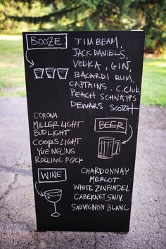 a black board with white writing on it sitting in front of a tree and grass area