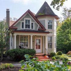 a house with white trim and brown shingles on the front porch, surrounded by greenery