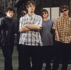 four young men standing in front of a building with their arms crossed and looking at the camera