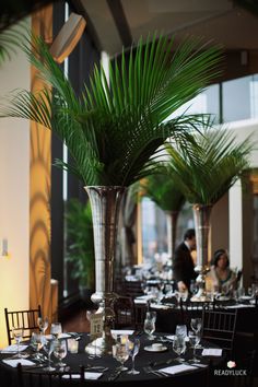 a tall vase filled with palm trees sitting on top of a black table cloth covered dining room