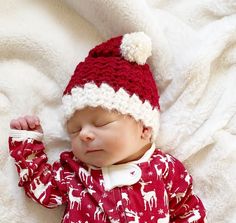 a baby wearing a red and white christmas outfit laying on a blanket with his eyes closed