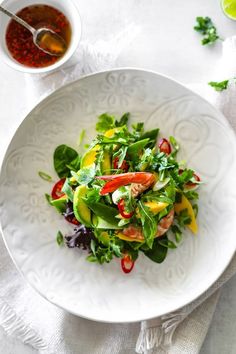 a white plate topped with salad next to a bowl filled with dressing and sauces