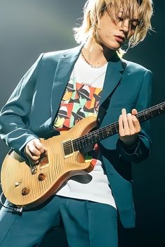 a man in a blue suit playing an electric guitar with blonde hair on his head