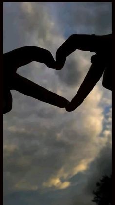 two hands in the shape of a heart against a cloudy sky with trees behind them