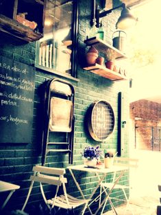 two chairs and a table in front of a green brick wall with writing on it