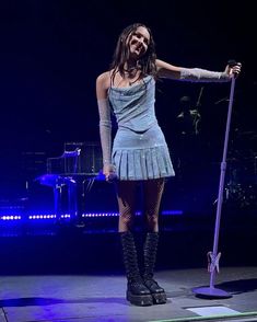 a woman in a short dress on stage with a microphone and an instrument behind her