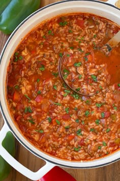 a large pot filled with beans and vegetables on top of a wooden table next to a spoon