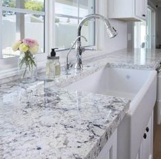 a kitchen with marble counter tops and white cabinets, along with an island style sink