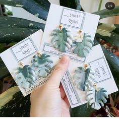 three green and white leaf shaped earrings sitting on top of each other in front of a plant