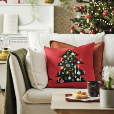 a christmas tree pillow sitting on top of a white couch next to a christmas tree