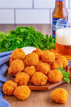 some fried food on a wooden board next to beer and parmesan cheese balls