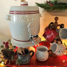 coffee mugs are sitting on a table with christmas decorations and lights in the background